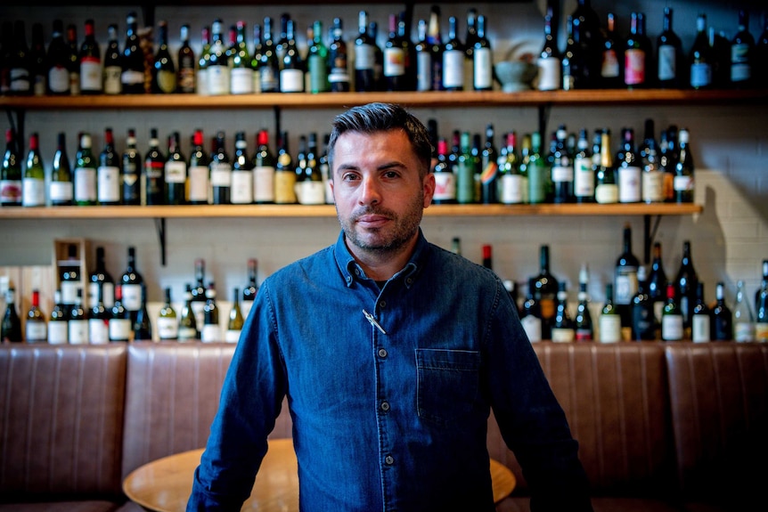 A man stands in front of a shelf filled with wine bottles