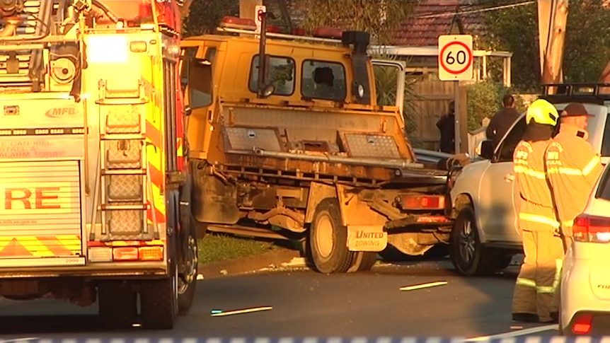 A yellow tow truck crashed into a tree, surrounded by emergency service workers.