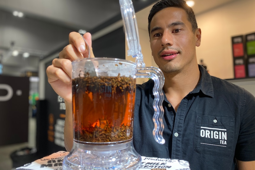 A man looks at a glass teapot filled with tea.