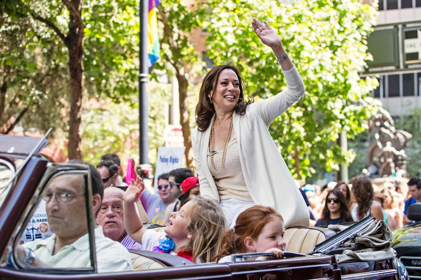 Kamala Harris sitting at the back of an open top car waving to the crowd