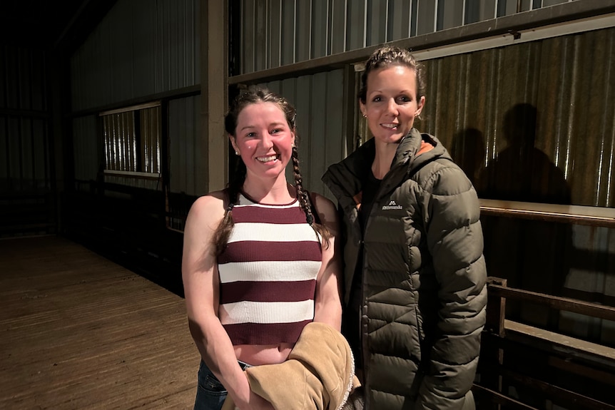 Two women stand in a shearing shed.