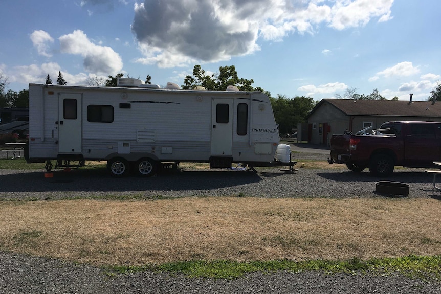 A maroon ute is seen parked in front of a caravan in front of what appears to be a motel in the US.