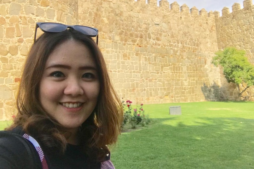 Dessy Widjaja smiles as she takes a selfie with a castle wall in the background.