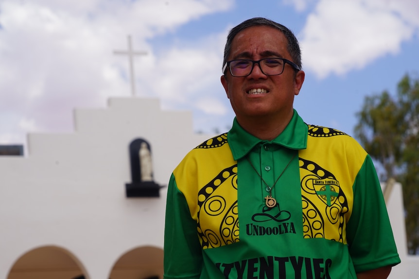 Santa Teresa Catholic Church parish priest Father Elmer Ibarra standing in front of the church and smiling at the camera.