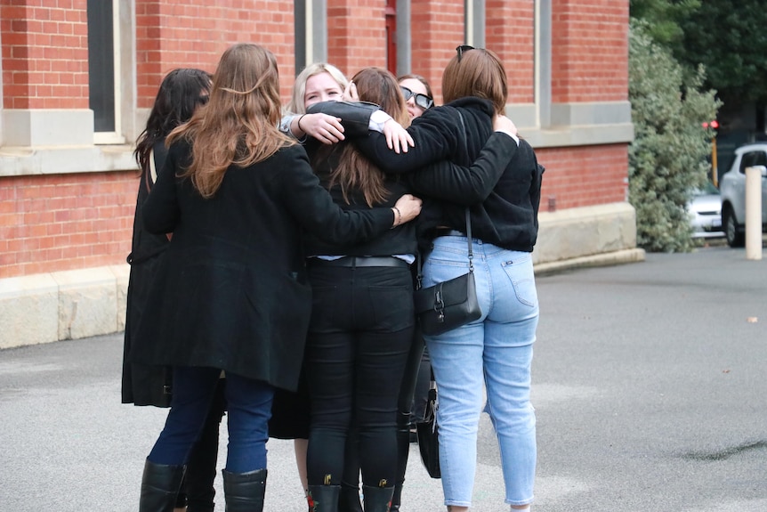 A group of women hug outside court