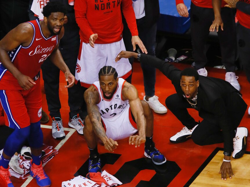 Kawhi Leonard, centre, sits down as Joel Embiid, left, leans and another man in a black shirt gasps, with his arms outstretched