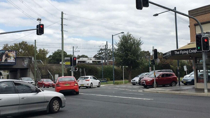 A set of traffic lights with several cars at it.