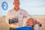 Man with a medical dummy holding an iPad with a video of the outback behind him.