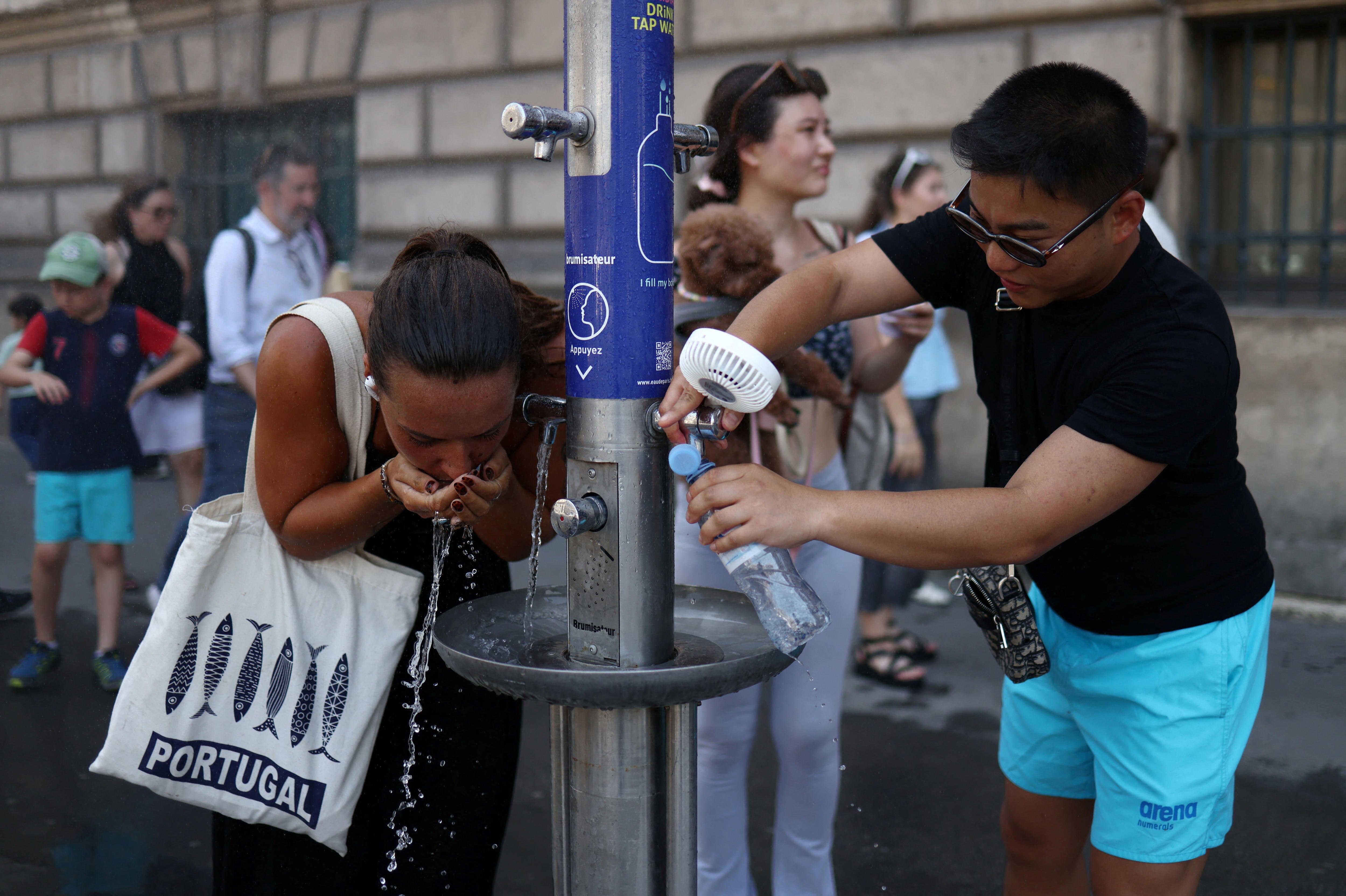 Tourists drink water and fill their water bottles at a city drinking fountain near the Louvre Museum