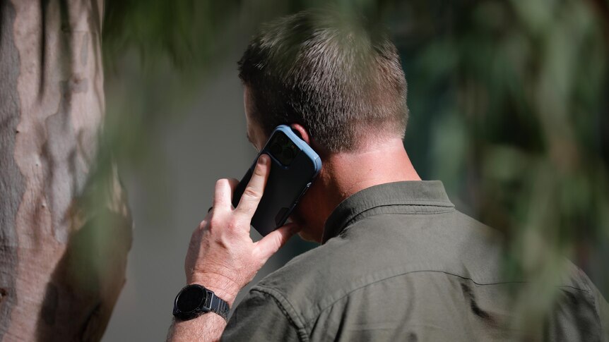 A man holds a phone to his ear, slightly obscured by gum leaves.