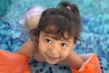 A young girl in the shallow end of the pool with floaties on her arms.