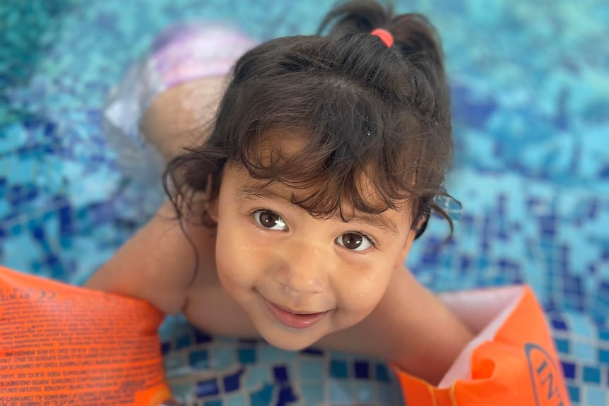 A young girl in the shallow end of the pool with floaties on her arms.