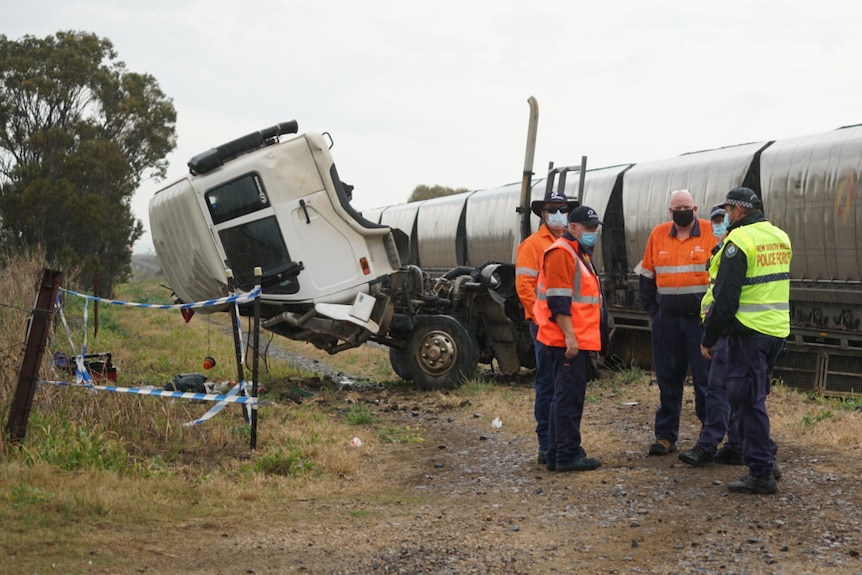 A truck with its cabin tipped over sits next to a coal train after a collision.