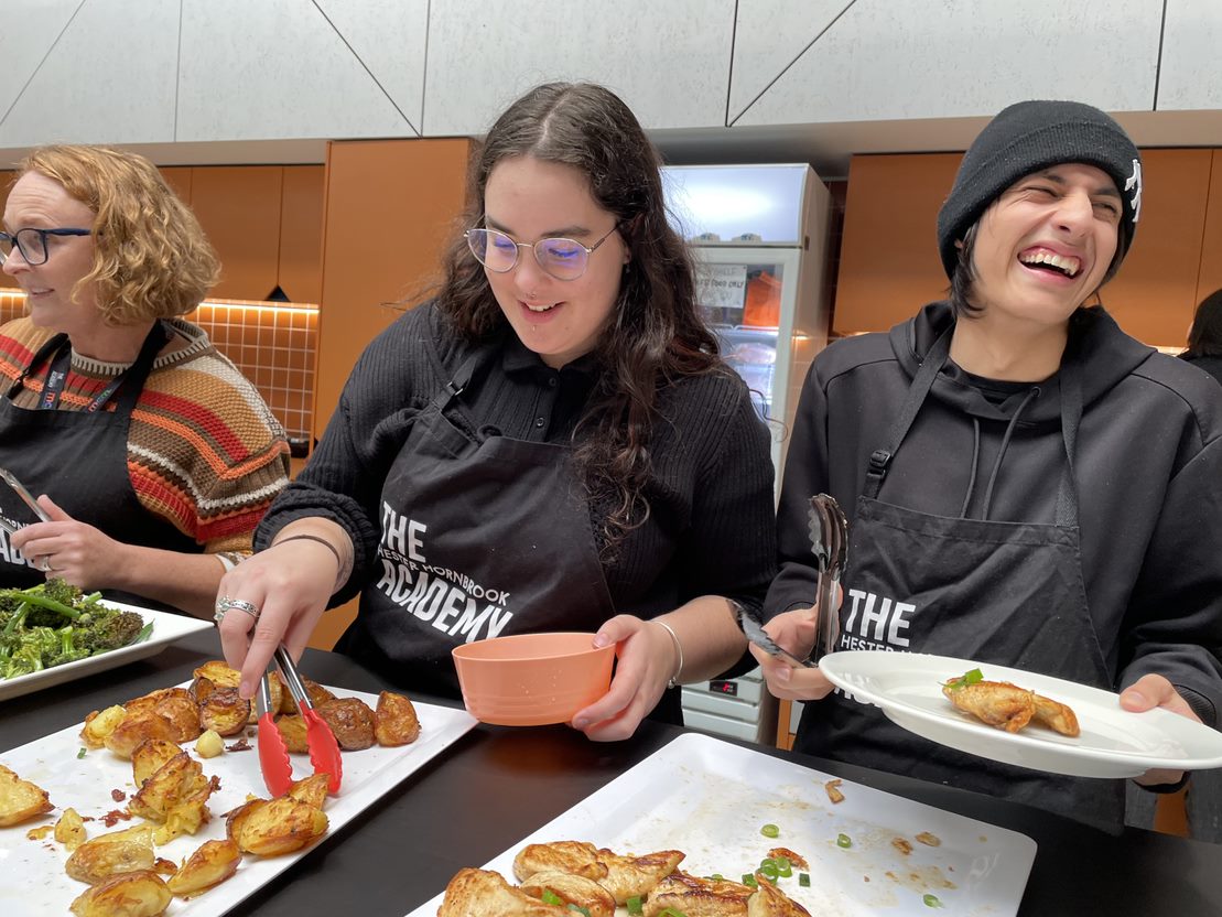 Three people serve a cooked lunch in the school kitchen.