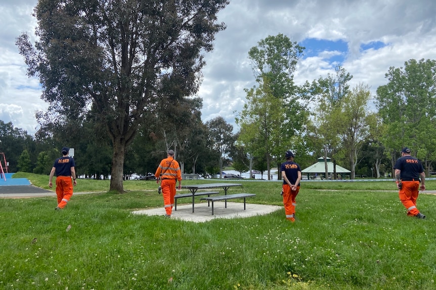 People wearing orange clothing walking in a line searching the ground. 