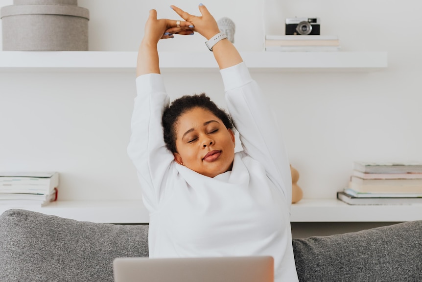 A woman stretching her arms, sitting in front of a computer, in her home.