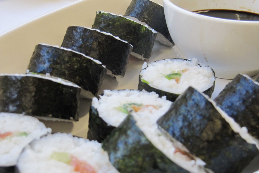 a line of sushi rolls lay on a plate next to a bowl of soy sauce