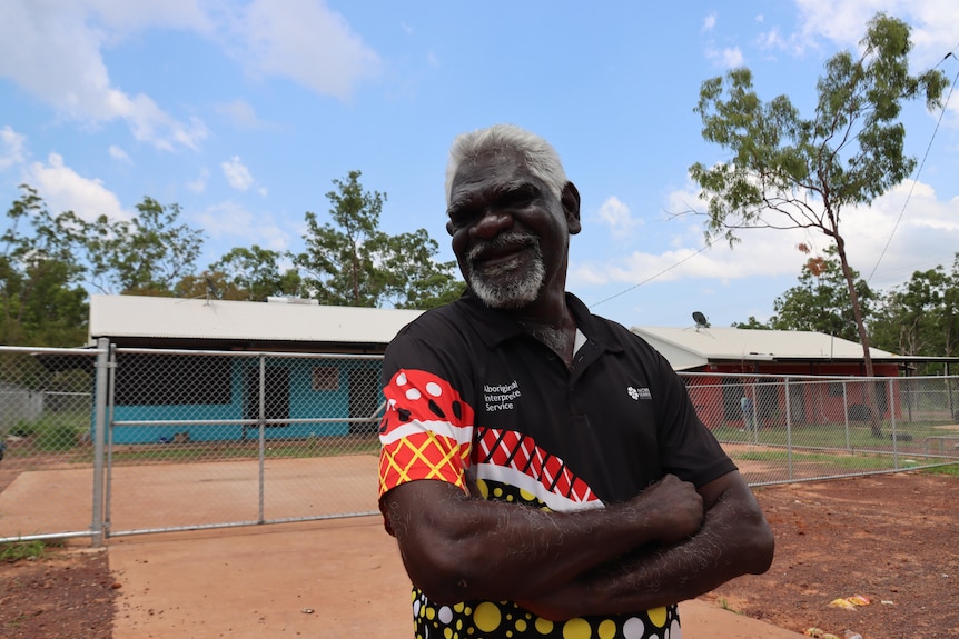 A photo of a happy man with white hair outside a small house in a remote community.
