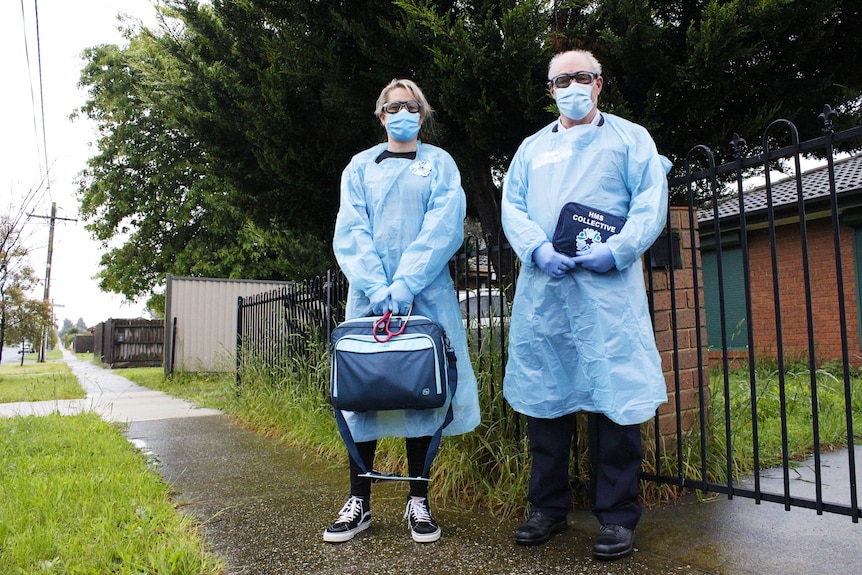 Two people in PPE outside a suburban home