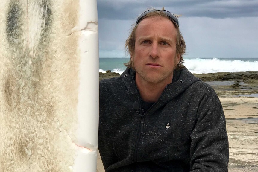 Surfer Marcel Brundler poses beside his surfboard with marks from the shark.