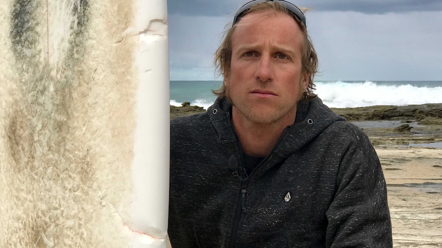 Surfer Marcel Brundler poses beside his surfboard with marks from the shark.