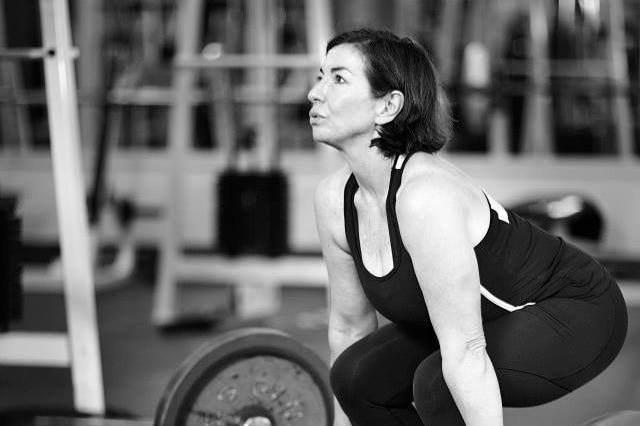 A woman in a black tank top lifting a heavy weight in a gym.