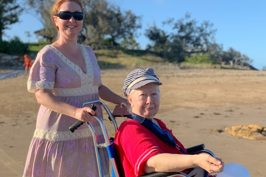 A woman pushing another woman in a wheelchair at the beach