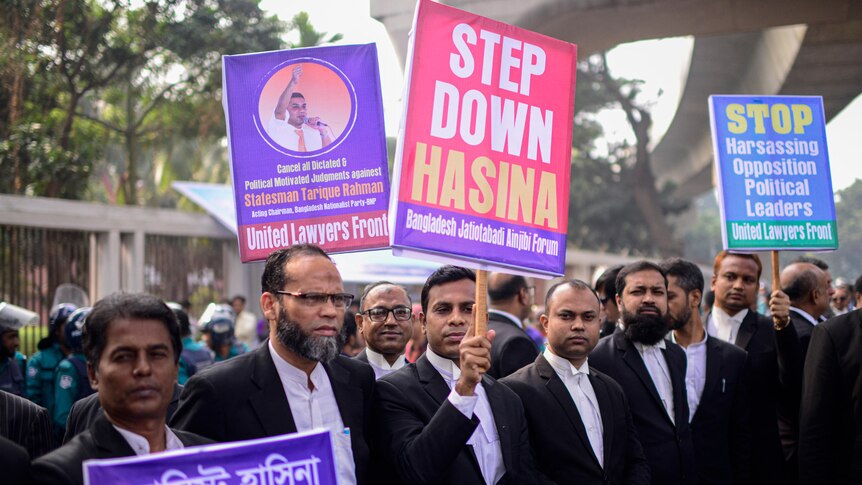 Men standing in a row holding protest signs against Bangladesh's Prime Minister, Sheikh Hasina.