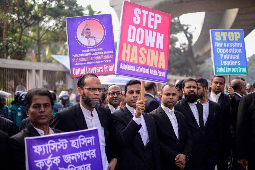 Men standing in a row holding protest signs against Bangladesh's Prime Minister, Sheikh Hasina.