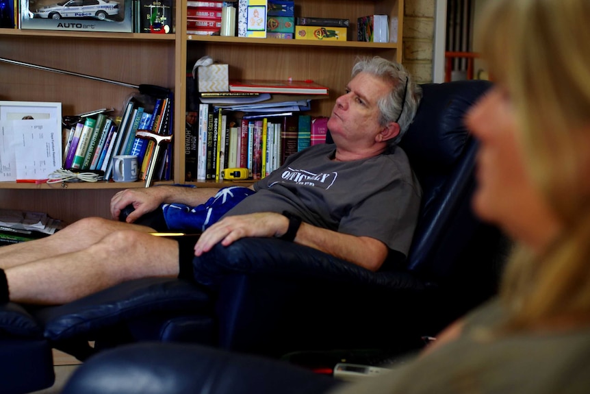 Tony Wallace sits in armchair his wife looks on.