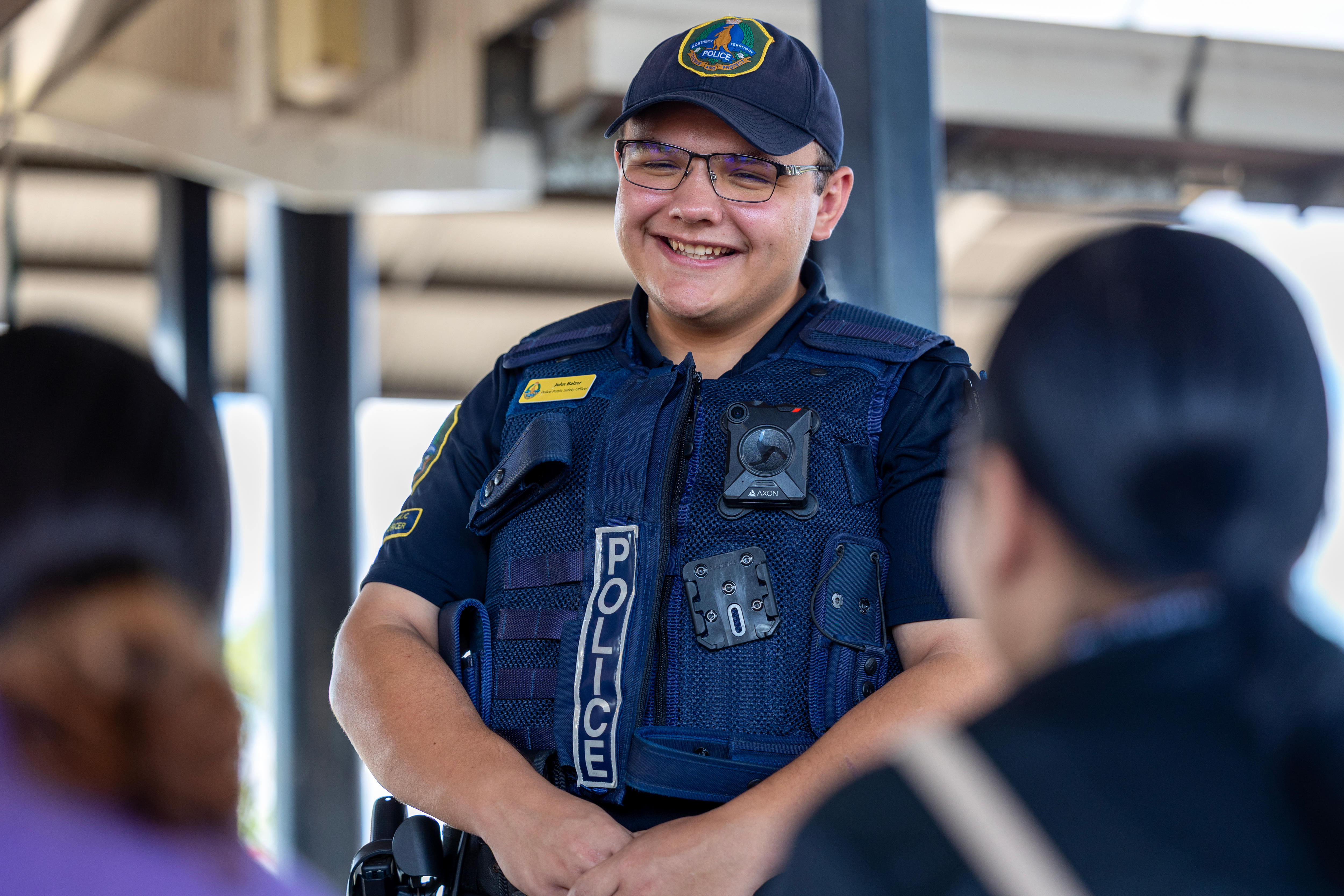 A police officer in uniform smiles at two members of the public.