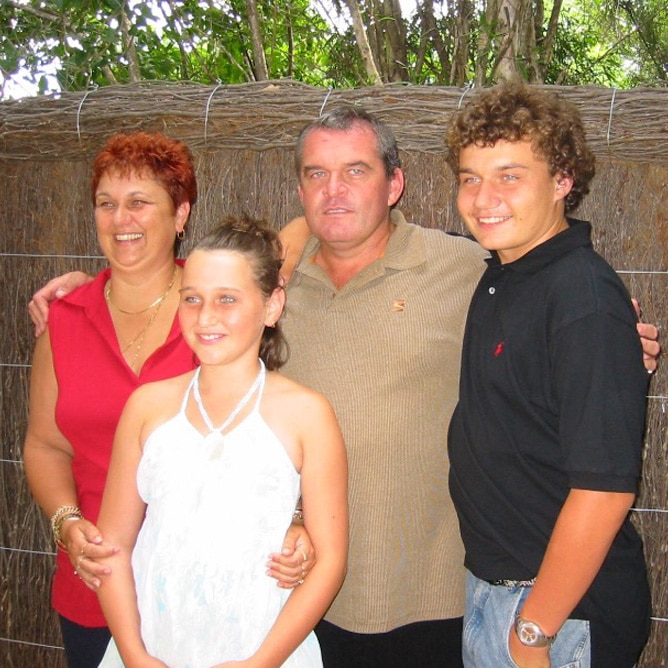 Family group photo: father, mother, son and daughter standing with their arms around each other.