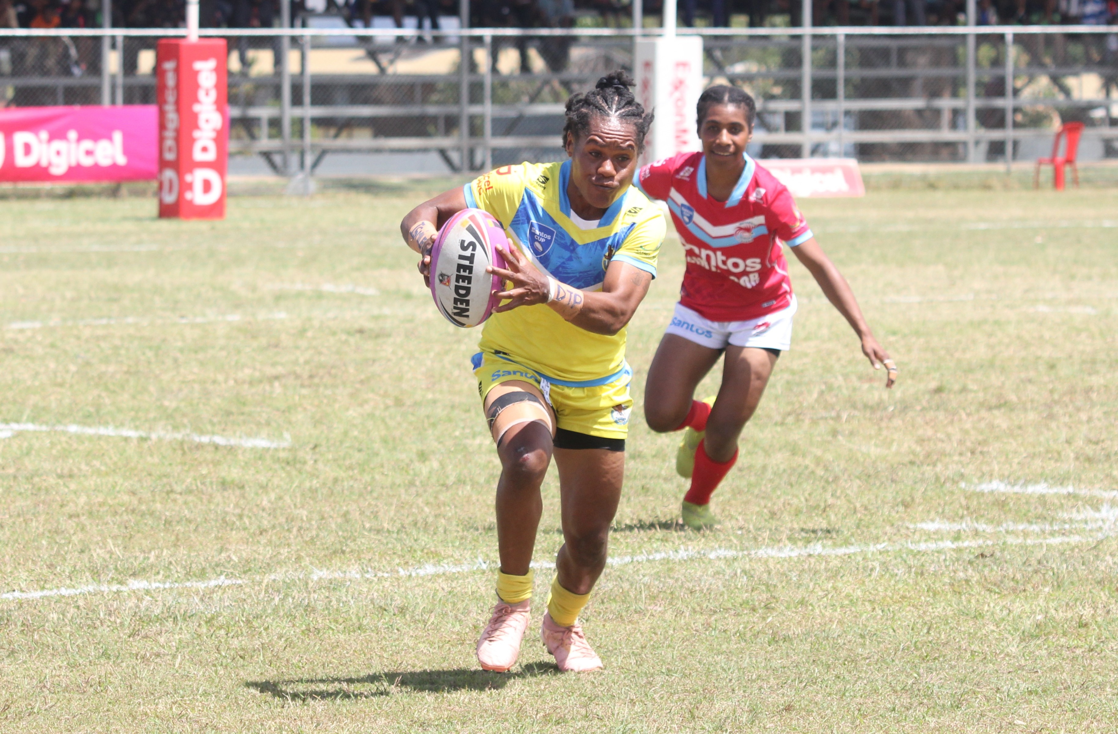 A woman wearing yellow runs with the football, chased by a player in red.