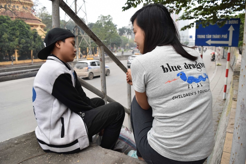 a young woman talks to a boy next to a Hanoi road
