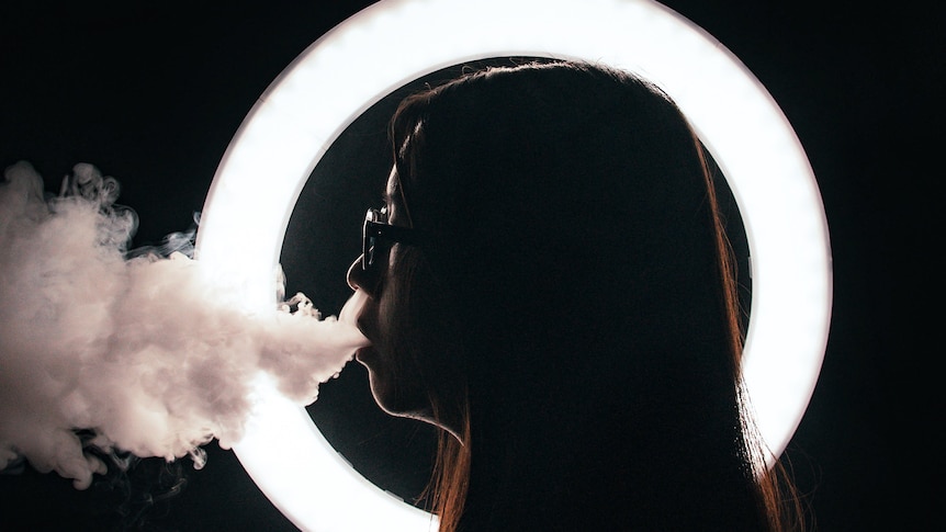 young woman with glasses vaping in dark room