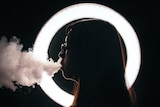 young woman with glasses vaping in dark room