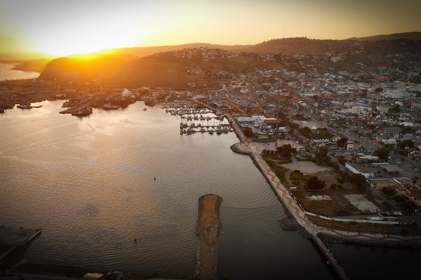 A drone shot over a city in Mexico where the sun sets behind a mountain.