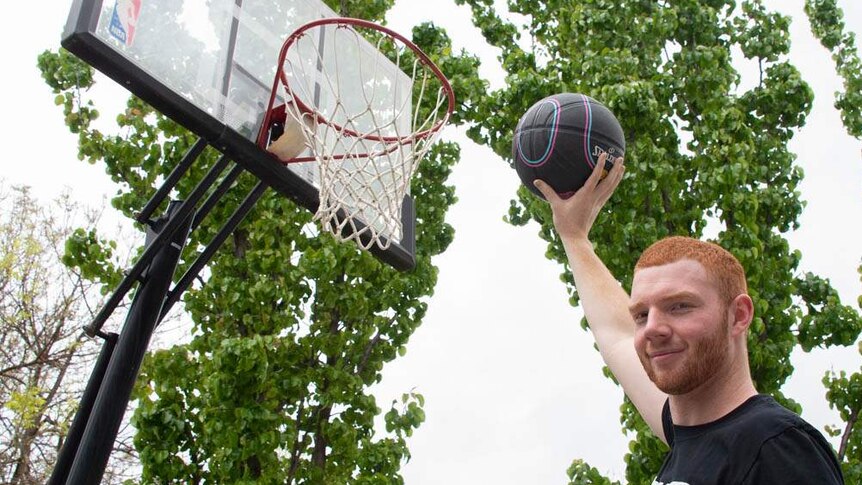 Angus Hartmann holding a basketball up to the hoop.