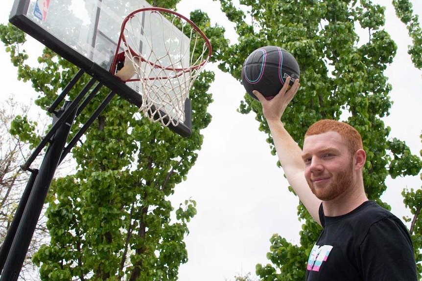 Angus Hartmann holding a basketball up to the hoop.