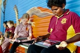 kids sitting on a school bench and looking at their ipads. 