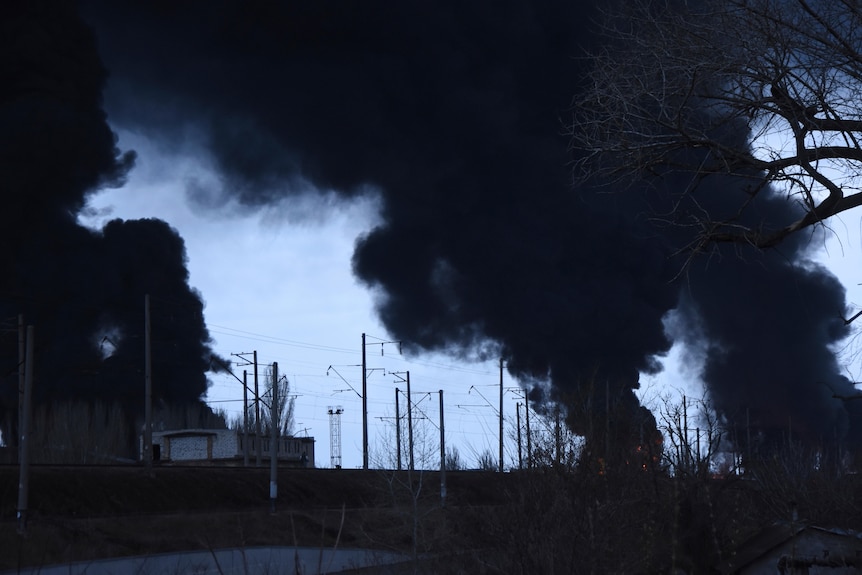 Smoke rises in the air against a dark sky from an urban area.