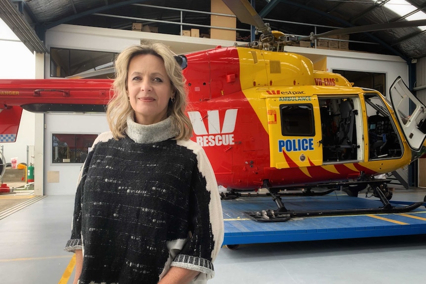 Pilot Allana Corbin stands in front of a rescue helictoper inside a hangar.