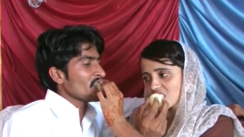 A woman in a veil feeds a man cake while he feeds her cake