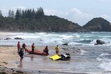 people near a life rafts and a jet ski on a wavy shore