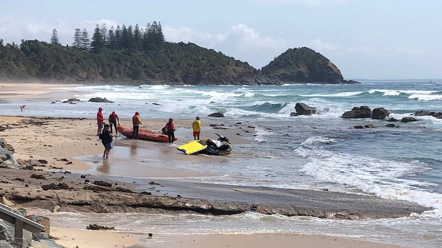 people near a life rafts and a jet ski on a wavy shore