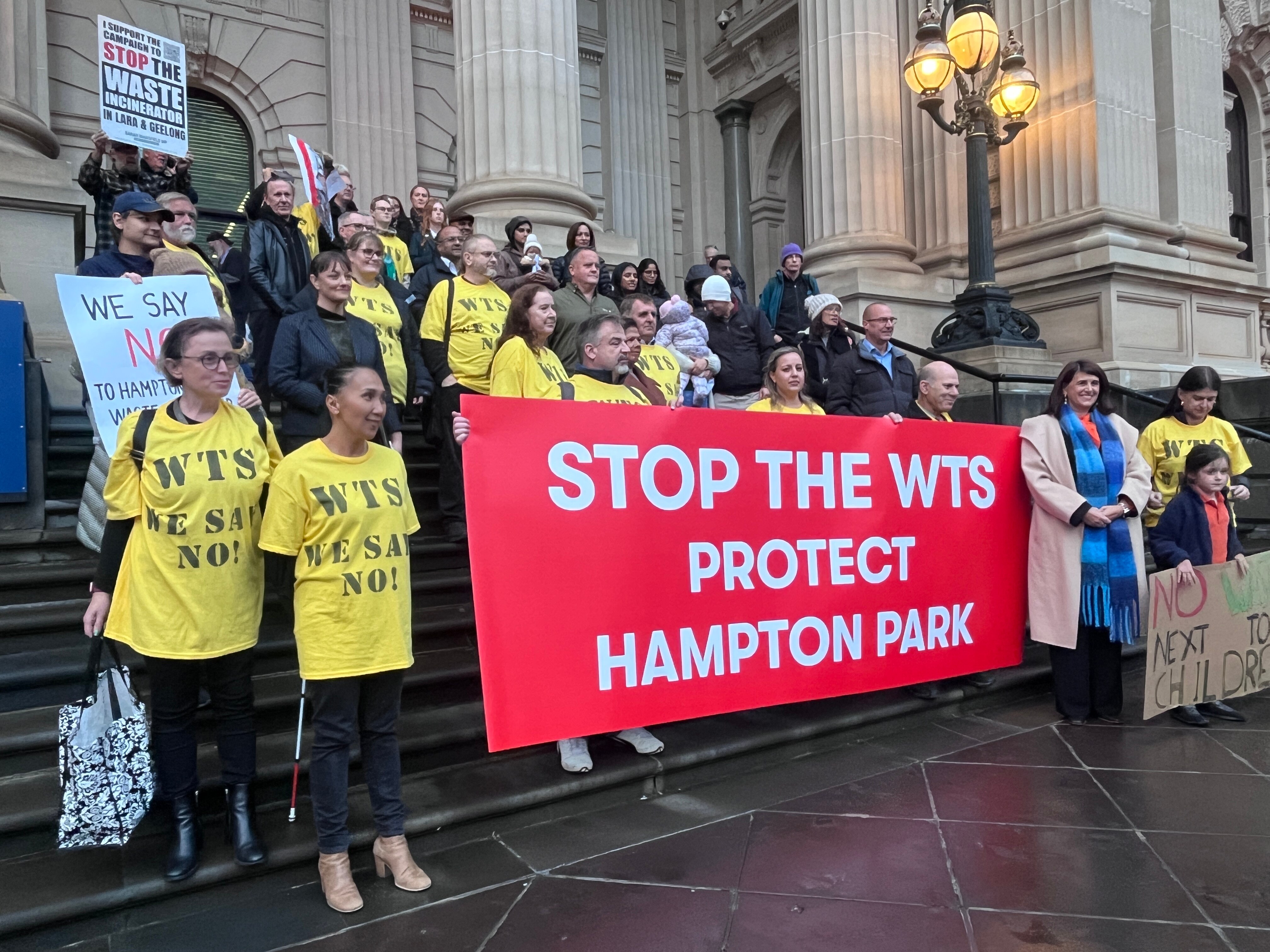Un grupo de manifestantes, muchos con camisas amarillas, de pie en los escalones de la Casa del Parlamento de Victoria.