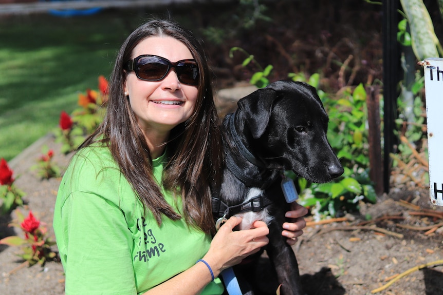 A woman wearing a green t-shirt smiles with a black dog. 