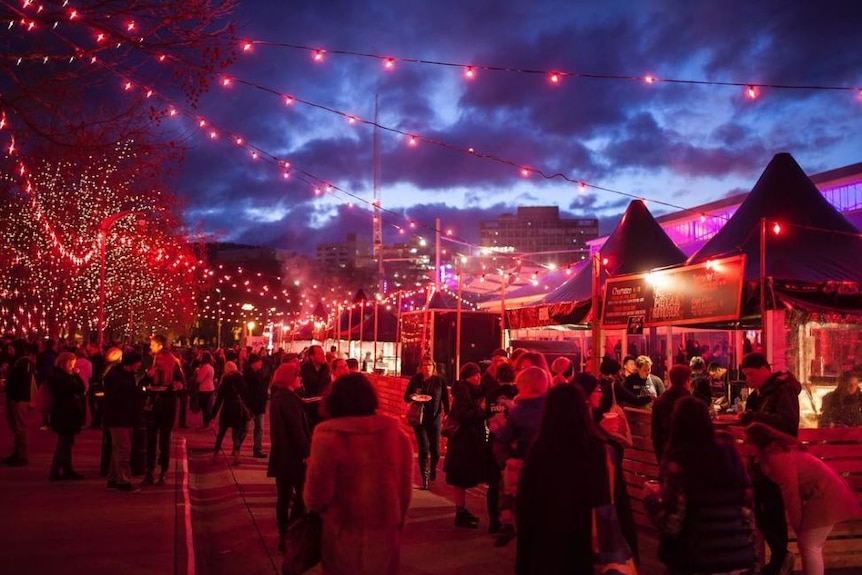 People mingle at outdoor festival event under lights.