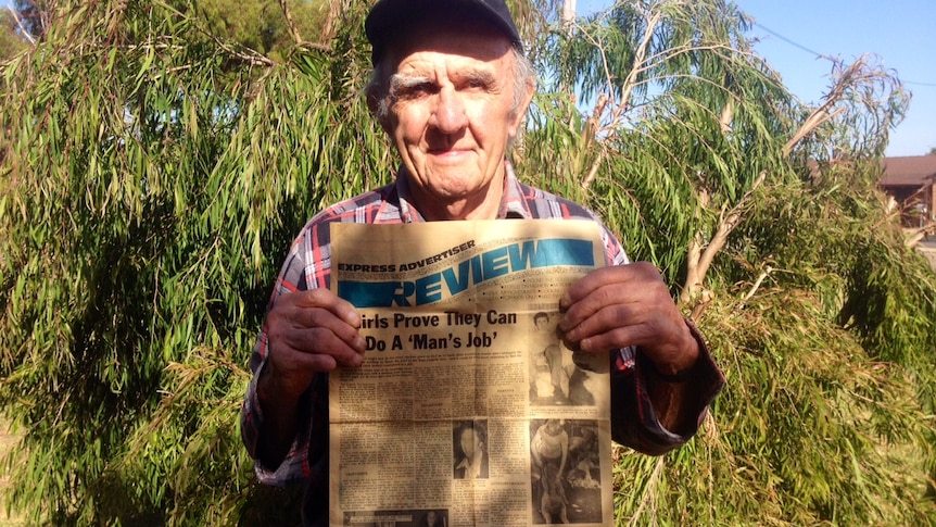 Man in chequered shirt holds old newspaper in front of tree in Esperance backyard