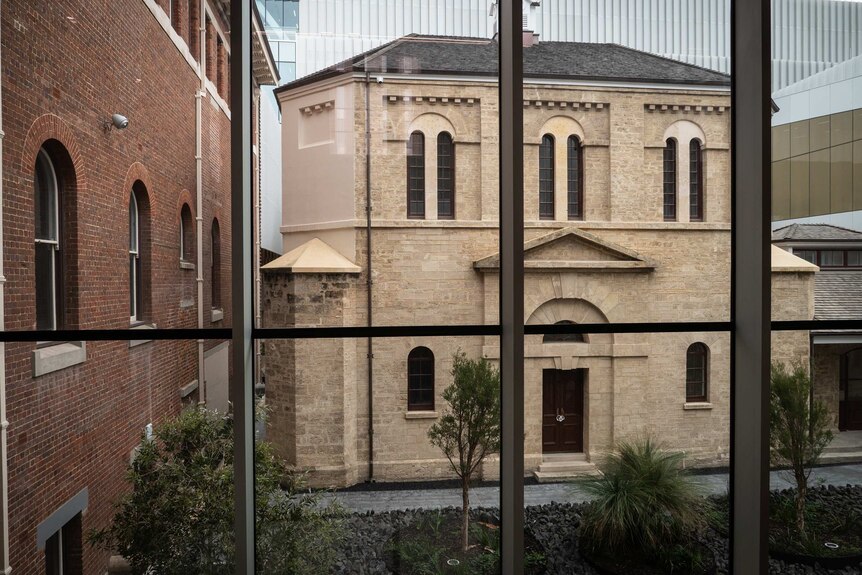 The old Perth gaol, seen through a glass window, surrounded by other buildings.